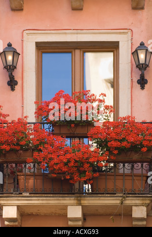 Veranda vor Glas Französisch Türen reflektieren blauen Himmel in einem rosa Stuck Gebäude mit einem Balkon mit roten Geranien Balkonkästen Stockfoto