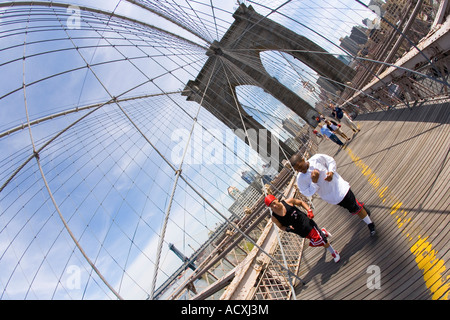 Brooklyn Bridge mit weißen und schwarzen männlichen Jüngling Jogger New York City bei Sonne Sonnenschein mit blauem Himmel Lower Manhattan downtown Stockfoto