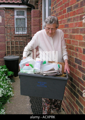 ältere Frau Außerbetriebnahme recycling Behälter gefüllt mit Zeitungen Kunststoffe für Curbside Sammlung Worthing West Sussex Stockfoto