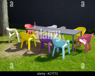 Neun farbige hell Kunststoffdesign Stühle um große graue Tisch im sonnigen Garten Stockfoto