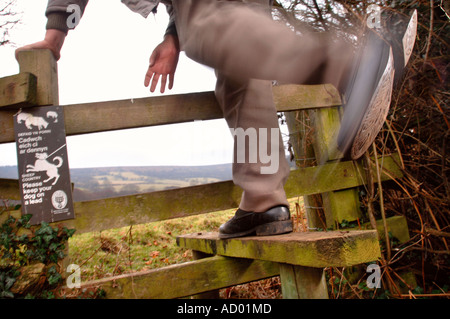 EIN PENSIONIERTER MANN SCHRITTE ÜBER EINEN HÖLZERNEN STIL MIT A HALTEN SIE BITTE IHREN HUND AUF EINEM BLEI SCHILD IN DER NÄHE VON ABERGAVENNY WALES UK Stockfoto