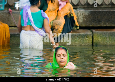 Horizontale Porträt einer indischen Frau halb untergetaucht in den Fluss Ganges und tief im Gebet in der Nähe von Kedar Ghat. Stockfoto