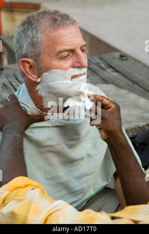 Horizontale Nahaufnahme eines westlichen Touristen, die eine Rasur von einem indischen Mann am Ufer des Flusses Ganges. Stockfoto