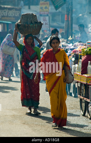 Vertikale Porträt von zwei lokalen indischen Frauen, die in der Regel Töpfe auf ihren Köpfen balancieren, während die Straße entlang. Stockfoto