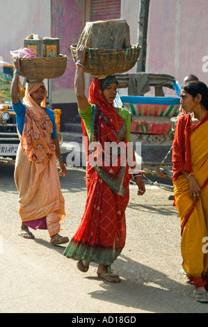Vertikale Porträt von zwei lokalen indischen Frauen, die in der Regel Körben und Töpfen auf dem Kopf balancieren, während die Straße entlang. Stockfoto