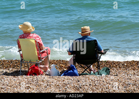 Älteres Ehepaar auf einem Meer Strand Rentner sitzen auf Stühlen entspannen Sie auf einem Kiesstrand in Südengland Stockfoto