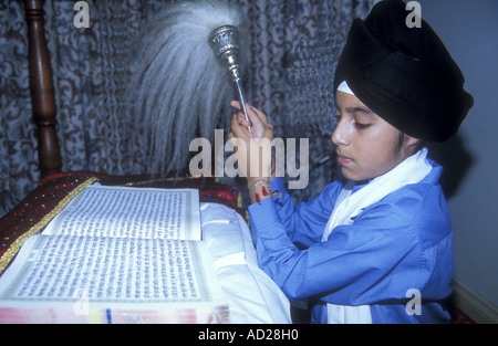 Der junge Sikh-Junge winkt mit dem Yak-Schwanz oder den Chauri über dem heiligen Guru Granth Sahib in einer Gurdwara Stockfoto