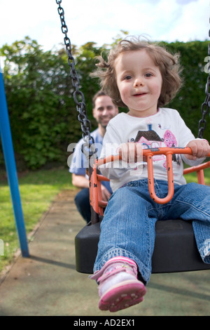 Kleines Mädchen auf der Schaukel auf dem Spielplatz im Park von Vater gedrängt Stockfoto