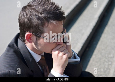 Junger Geschäftsmann legt seine Hand zum Mund, als er in der Londoner City Handy benutzt Stockfoto