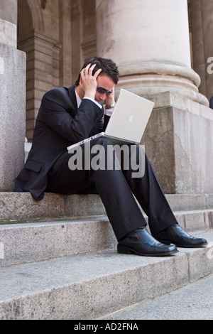 Junger Geschäftsmann legt die Hände an den Kopf, als er auf seinem Laptop in der City of London Finanzdaten anschaut Stockfoto