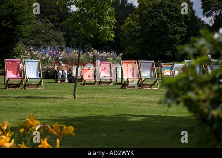 Ein Mann sitzt auf seinen eigenen Zeitunglesen umgeben von Multi farbige Liegestühle im Regents Park London UK Stockfoto