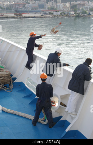 Kreuzfahrt-Liner-Andockverfahren Seemann warf gewichtete Kugel und dünne starke Linie an Land, verbunden mit schweren Festmacherseilen, benutzte Hafenarbeiter, um das Schiff zu sichern Stockfoto