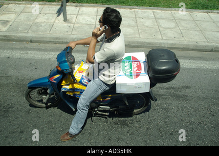 Athen-Mann auf Roller warten an der Ampel im Chat auf Handy Fahrrad beladen mit Beutel der Späne Stockfoto