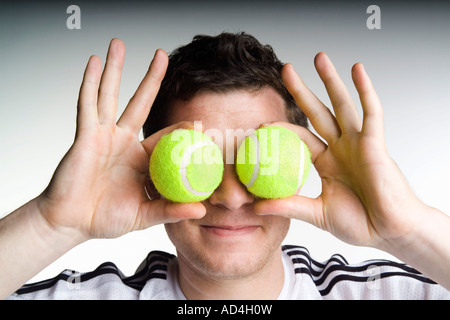 Ein Mann, der zwei Tennisbälle vor sein Gesicht hält Stockfoto