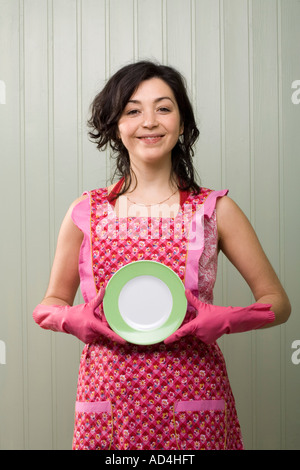 Eine Frau hält einen Teller während einer Schürze und Gummihandschuhe tragen Stockfoto