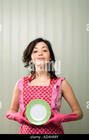 Eine Frau hält einen Teller während einer Schürze und Gummihandschuhe tragen Stockfoto