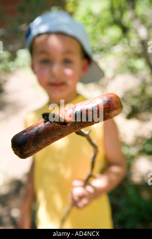 Ein kleiner Junge hält eine gekochte Wurst auf einem stick Stockfoto