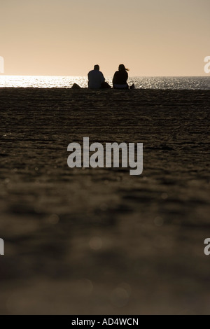 Ein paar sitzt am Strand bei Sonnenuntergang Stockfoto