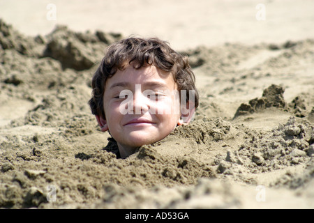 Kleine Junge vergraben im Sand mit seinem Kopf ragte aus Stockfoto