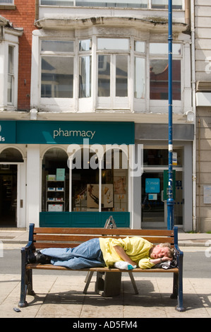 betrunken Obdachloser schläft auf einer Bank in der Straße Aberystwyth Stockfoto