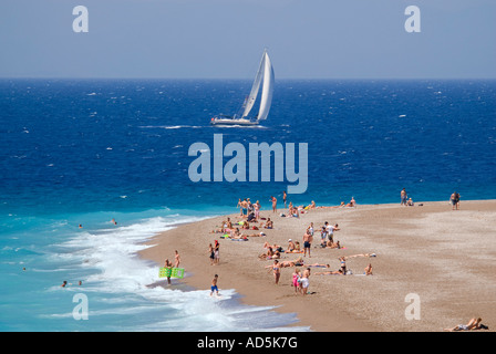 Horizontale Luftaufnahme von Urlaubern am Strand mit einem weißen Yacht Segeln bestanden in der Sonne. Stockfoto