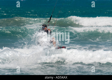 Horizontale Nahaufnahme von kaukasischen männlichen Kitesurfer in einer hockenden Position krachend durch die Wellen Stockfoto