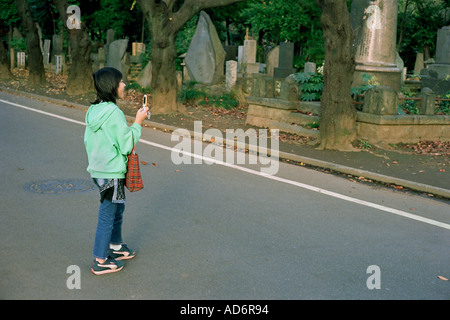 Ein Teenager nutzt ihr Handy, ein Bild auf einem Friedhof in Tokio Stockfoto
