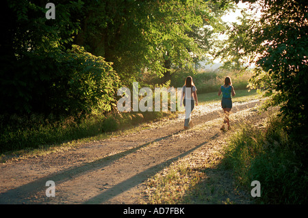 Zwei junge kaukasische Frauen gehen in den Sonnenaufgang in der auf einem Feldweg in den Park, mit Schatten hinter ihnen. Stockfoto