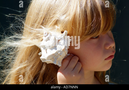 Kleines Mädchen hält eine Muschel zu ihrem Ohr hört zu den Klängen von Meer Stockfoto