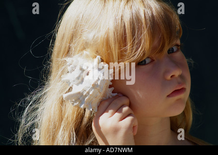 Kleines Mädchen hält eine Muschel zu ihrem Ohr hört zu den Klängen von Meer Stockfoto