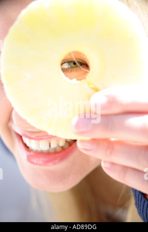 Porträt der jungen Frau mit Ananasscheibe vor einem Auge, Lächeln Stockfoto