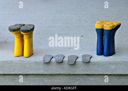 Gelbe und blaue Stiefel auf dem Kopf stehend links an einem grauen, die konkrete Veranda zum trockenen Einlegesohlen dazwischen fein säuberlich aufgereiht Stockfoto