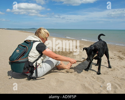 Frau spielt mit einem schwarzen Hund am Strand Stockfoto