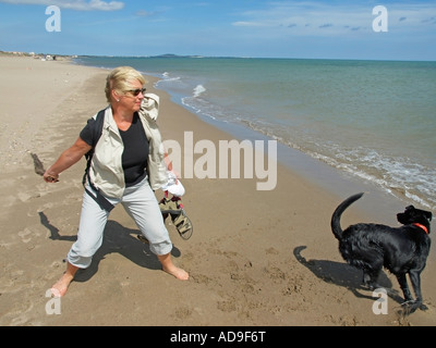 Frau spielt mit einem schwarzen Hund am Strand Stockfoto