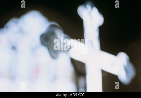 Klangschöne nahe gewölbt bis eine reflektierende Silber Kruzifix kontrastiert eine leichte Glasmalerei Fenster und eine dunkle Wand Stockfoto