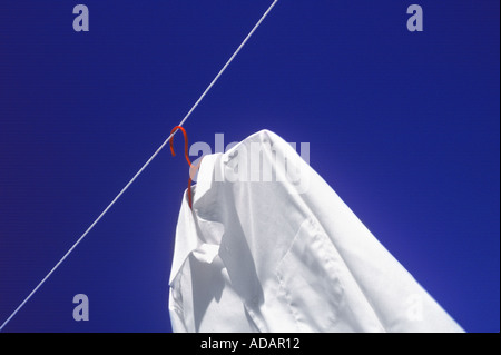 Weißes Hemd und eine rote Bügel auf Wäscheleine mit blauem Himmel Stockfoto