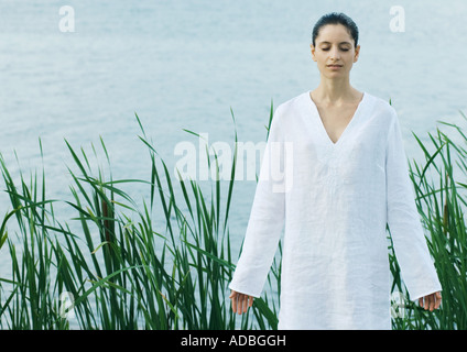 Frau stehend mit Armen, in der Nähe von Wasser, Augen geschlossen Stockfoto