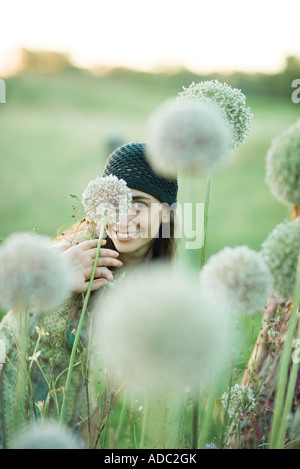 Junge Frau versteckt sich hinter Allium Blume, Blick in die Kamera Stockfoto