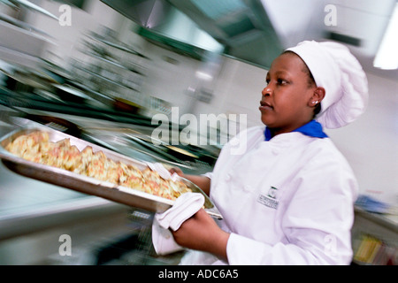 Eine junge schwarze Köchin hält ein Tablett mit zubereiteten Speisen in der Küche Stockfoto