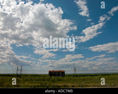 ein verfallenes Graffitied Gebäude steht allein im Offenland unter blauem Himmel mit weißen Wolken punktiert Stockfoto