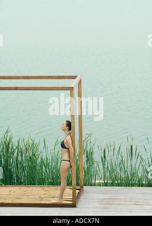 Frau mit Bikini, stehend in Holzkonstruktion, in der Nähe von See Stockfoto