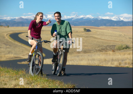 Lächelnd mittleren Paar Fahrrad fahren auf einem Pfad mit Bergkette in den Hintergrund Frauen Punkten im Alter von Stockfoto