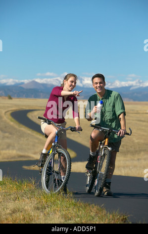 Lächelnd mittleren Paar Fahrrad fahren auf einem Pfad mit Bergkette in den Hintergrund Frauen Punkten im Alter von Stockfoto