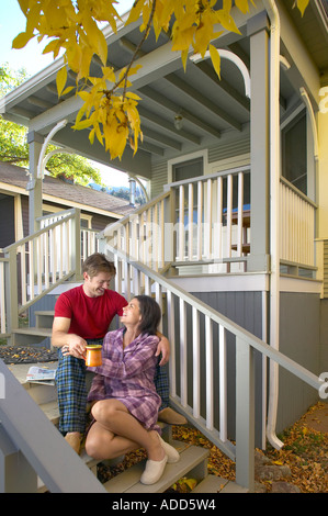 Paar im Pyjama sahen einander sitzt mit Kaffee und Papier auf Holztreppen einer Hütte im Herbst Stockfoto