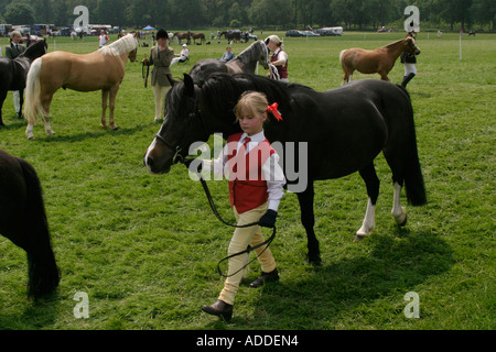 Ein junges Mädchen in rot geht mit ihrem Pony während eines Wettkampfes auf dem South Oxfordshire Riding Club Open Show Stockfoto