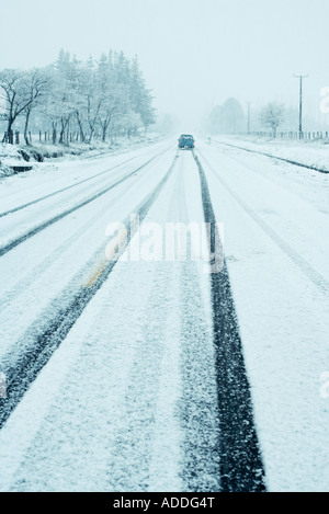 Auto auf der Straße, die durch tief verschneite Landschaft Stockfoto