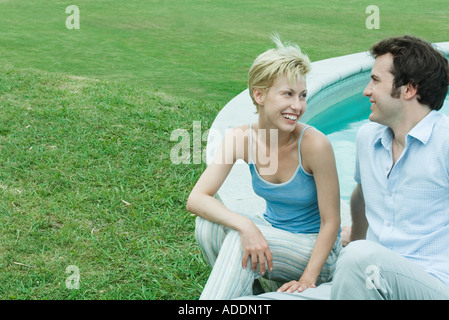 Paar von Edge of Pool, mit Blick auf einander, lächelnd sitzt Stockfoto