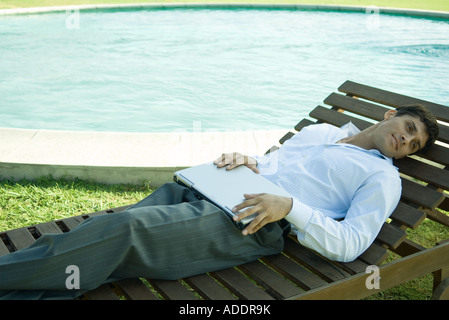 Geschäftsmann im Liegestuhl in der Nähe von Pool, Runde Laptop festhalten Stockfoto