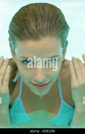 Junge Frau im Pool, die Hände von Seite des Gesichts und Gesicht tropft Stockfoto