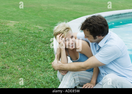 Paar sitzt Pool, Lächeln einander an Stockfoto